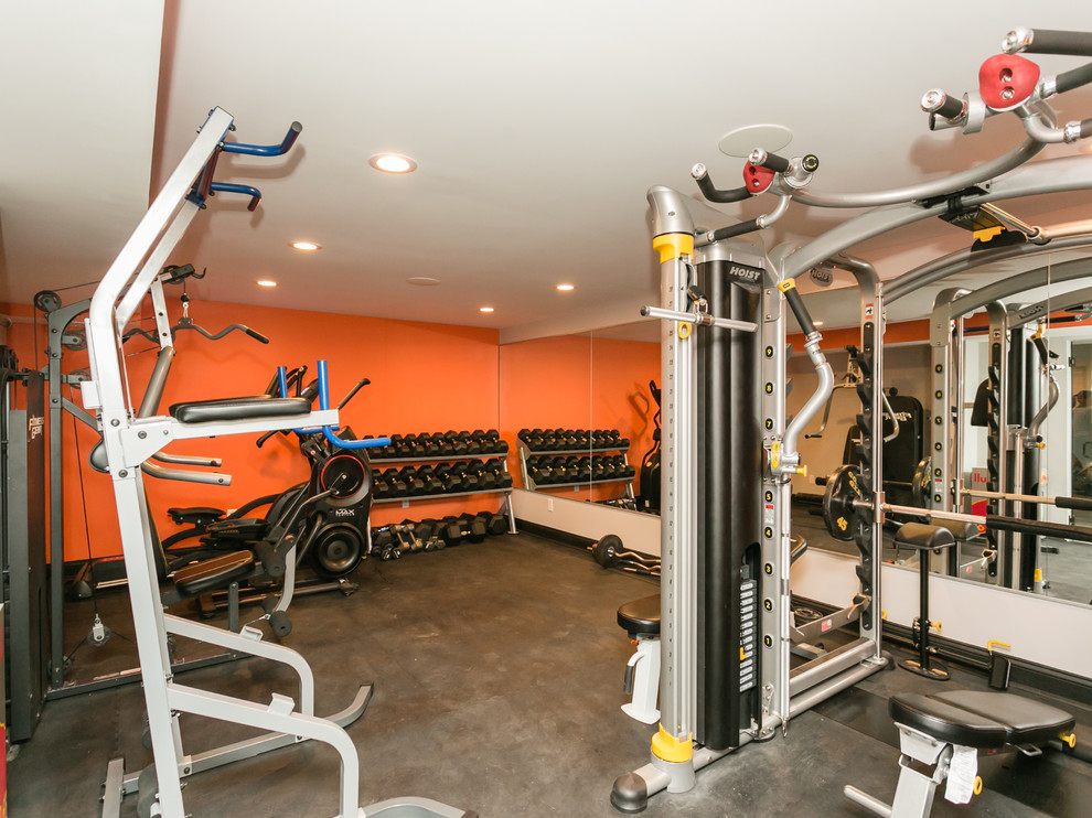 На фото: домашний тренажерный зал в стиле модернизм с тренажерами, оранжевыми стенами и черным полом с