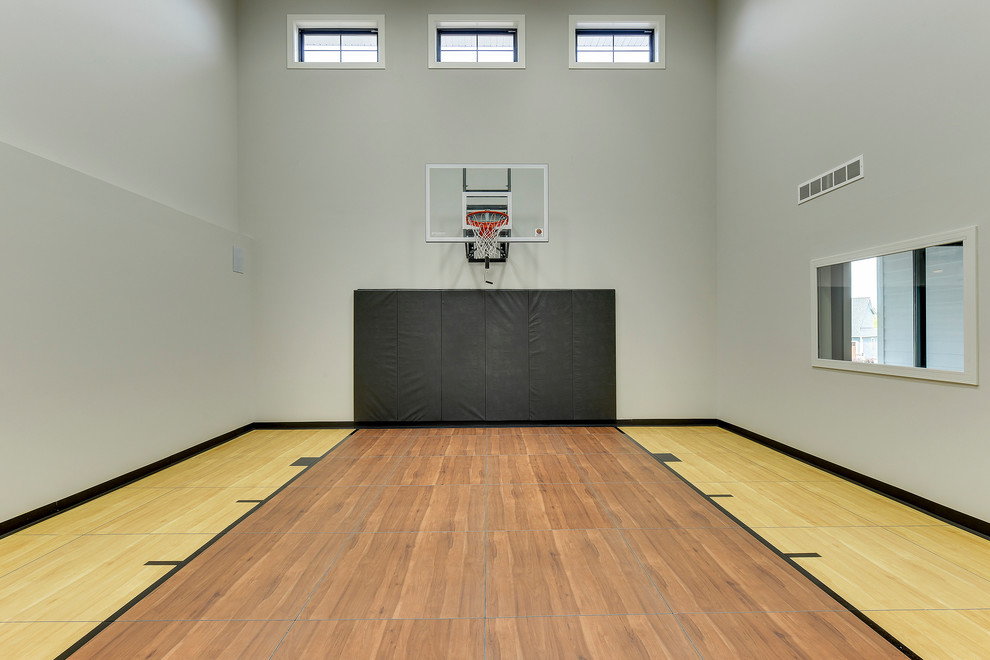Imagen de pista deportiva cubierta de estilo de casa de campo grande con paredes grises, suelo marrón y suelo de madera en tonos medios