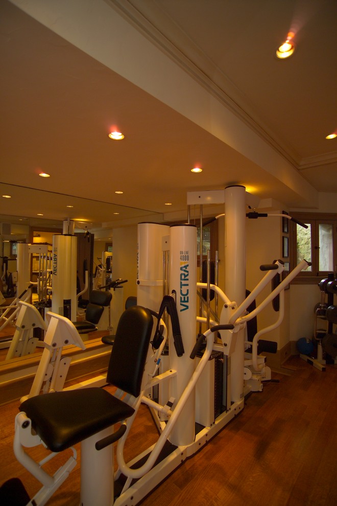 Exemple d'une grande salle de musculation chic avec un mur beige et un sol en bois brun.