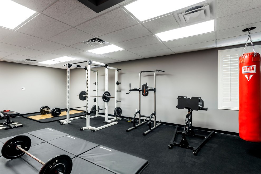 Diseño de sala de pesas minimalista grande con paredes grises y suelo negro