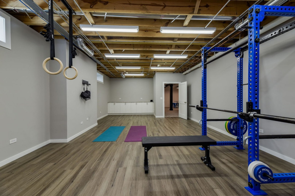 Modelo de gimnasio multiusos tradicional renovado de tamaño medio con paredes grises, suelo laminado y suelo marrón