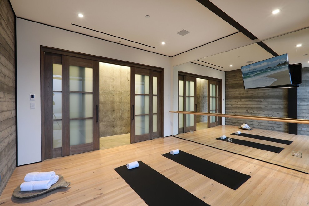 Ejemplo de estudio de yoga actual de tamaño medio con paredes grises, suelo de madera clara y suelo marrón