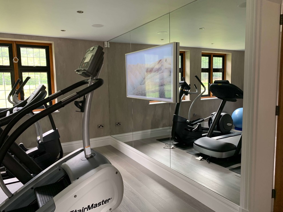 This is an example of a medium sized contemporary home weight room in Hertfordshire with grey walls, painted wood flooring and beige floors.