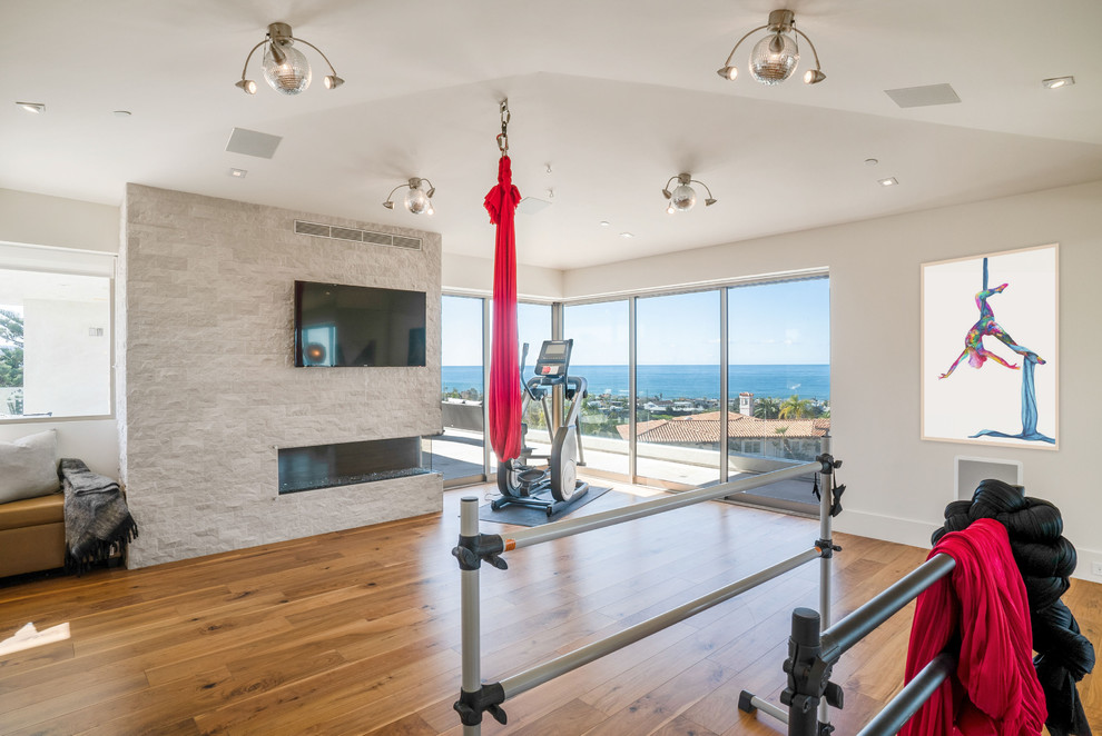 Large trendy medium tone wood floor and brown floor multiuse home gym photo in Los Angeles with white walls