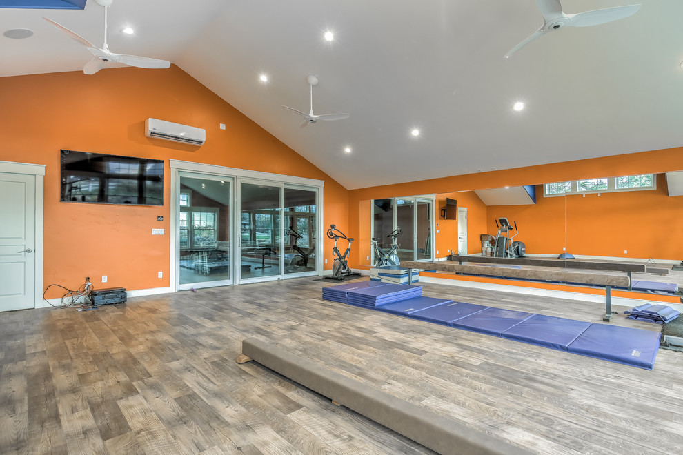Exemple d'une grande salle de sport chic multi-usage avec un mur orange et un sol en bois brun.
