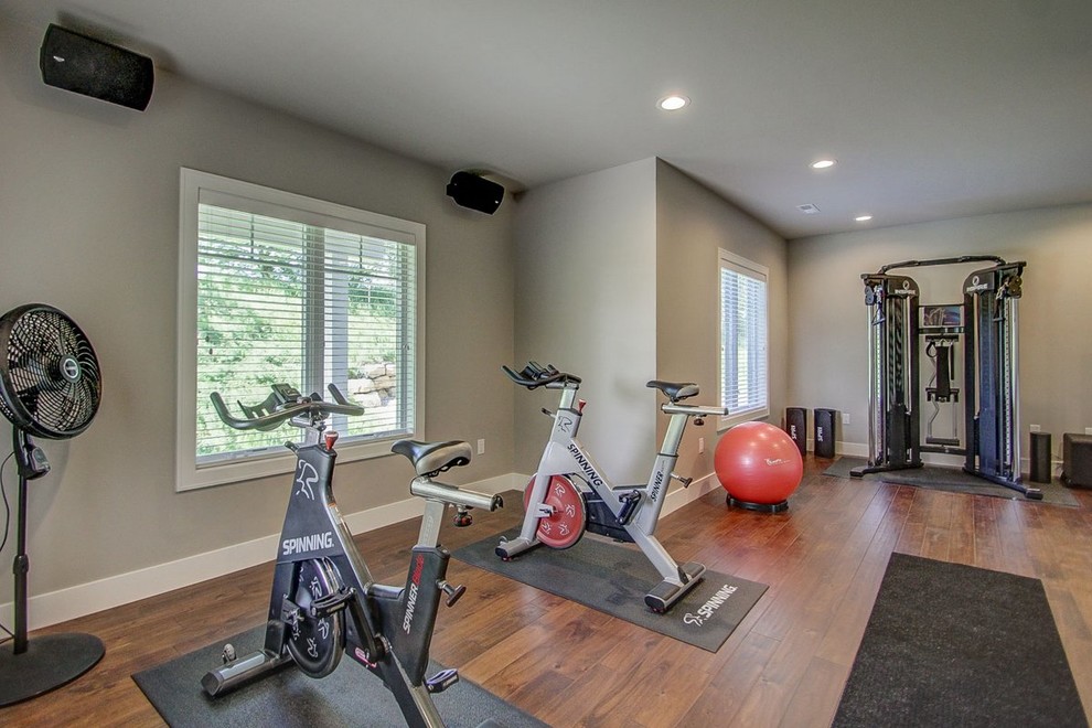 Großer Klassischer Fitnessraum mit grauer Wandfarbe und braunem Holzboden in Sonstige