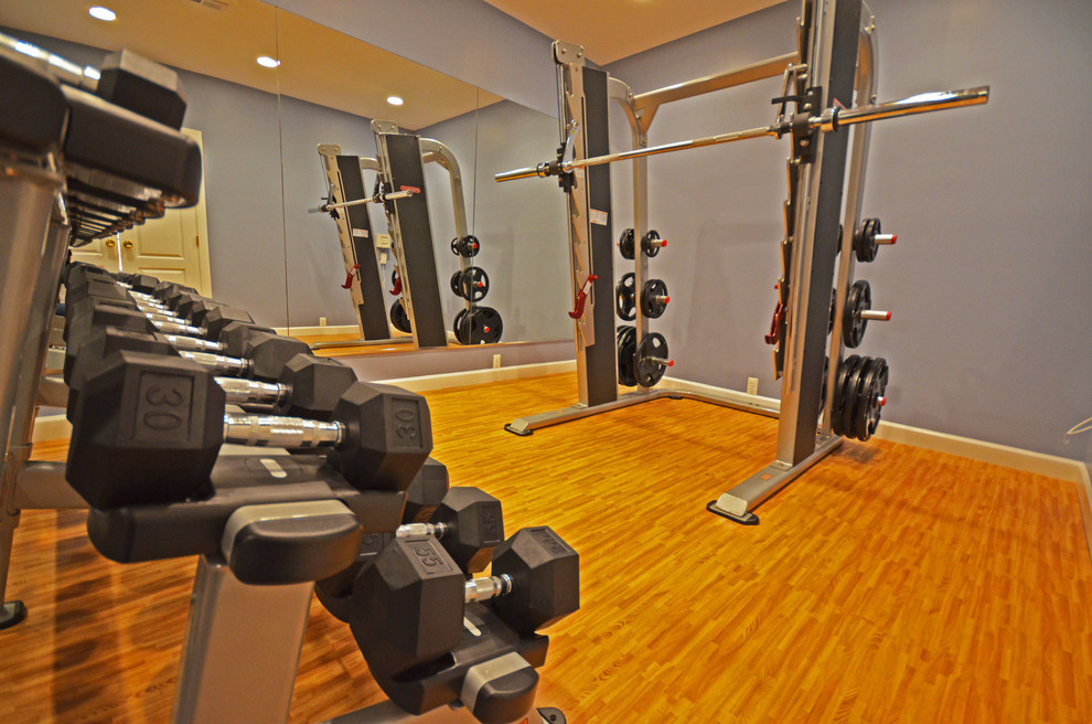 На фото: домашний тренажерный зал среднего размера в классическом стиле с тренажерами, синими стенами, полом из бамбука и коричневым полом