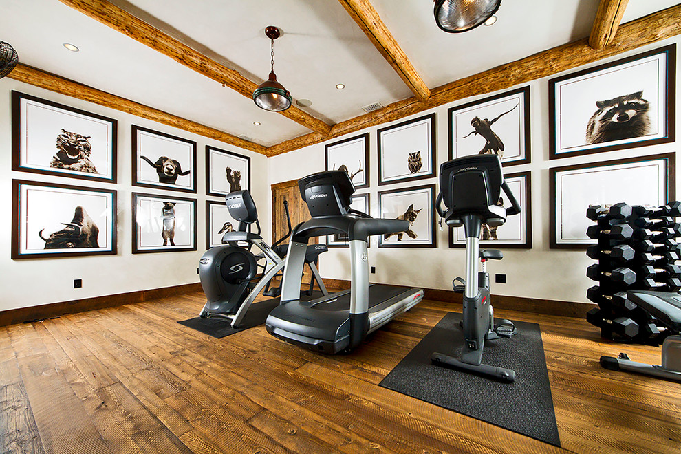 Rustikaler Fitnessraum mit weißer Wandfarbe, braunem Holzboden und braunem Boden in Sonstige
