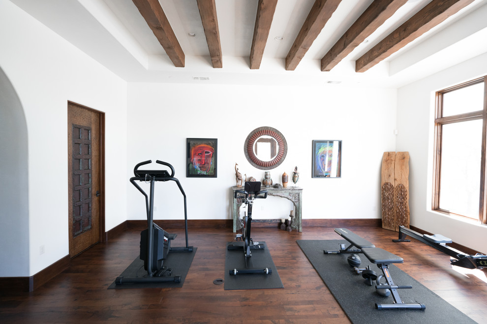 Multifunktionaler Mediterraner Fitnessraum mit dunklem Holzboden, weißer Wandfarbe und braunem Boden in Austin