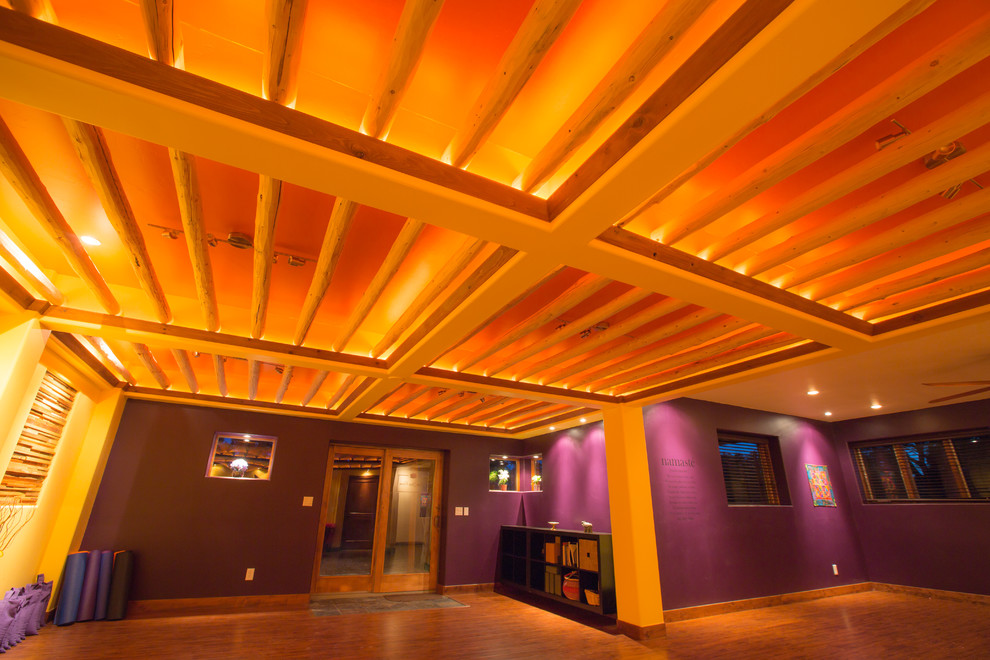 Cette image montre un grand studio de yoga chalet avec un mur violet, un sol en bois brun et un sol marron.