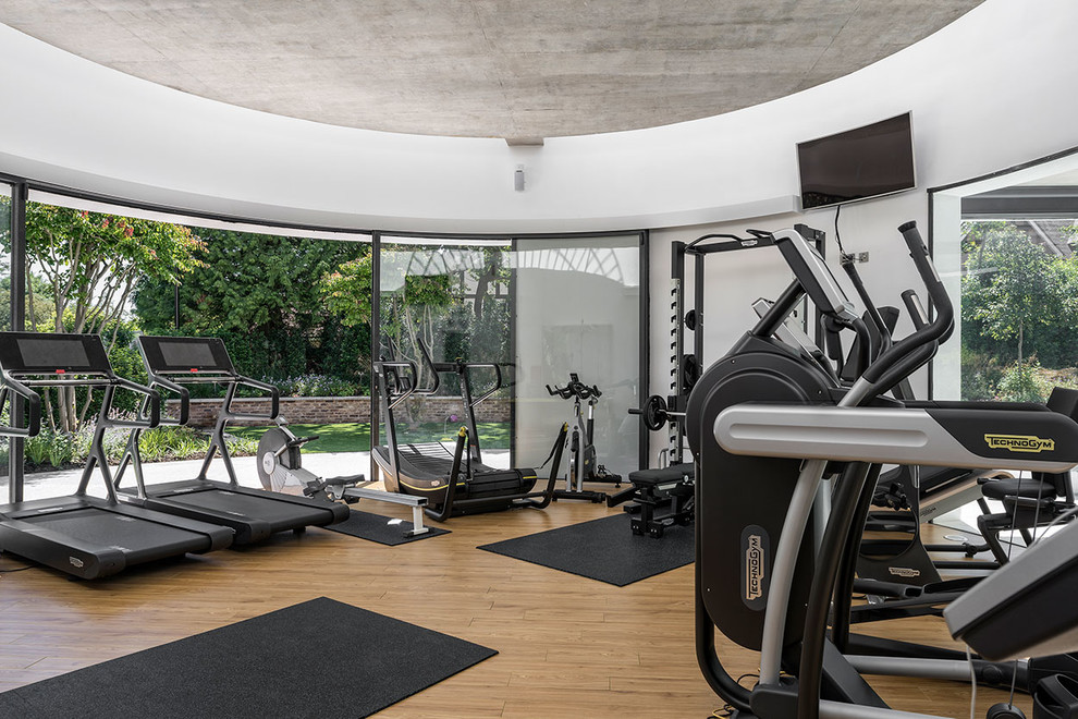 Multifunktionaler Moderner Fitnessraum mit weißer Wandfarbe und braunem Holzboden in London