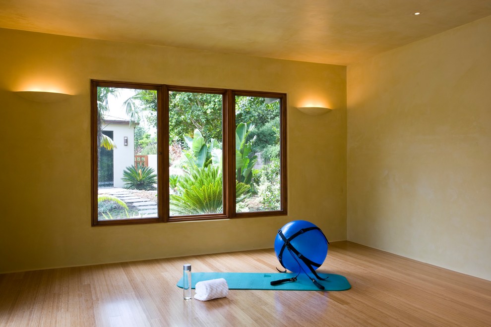Diseño de estudio de yoga tropical de tamaño medio con paredes beige, suelo de madera clara y suelo beige
