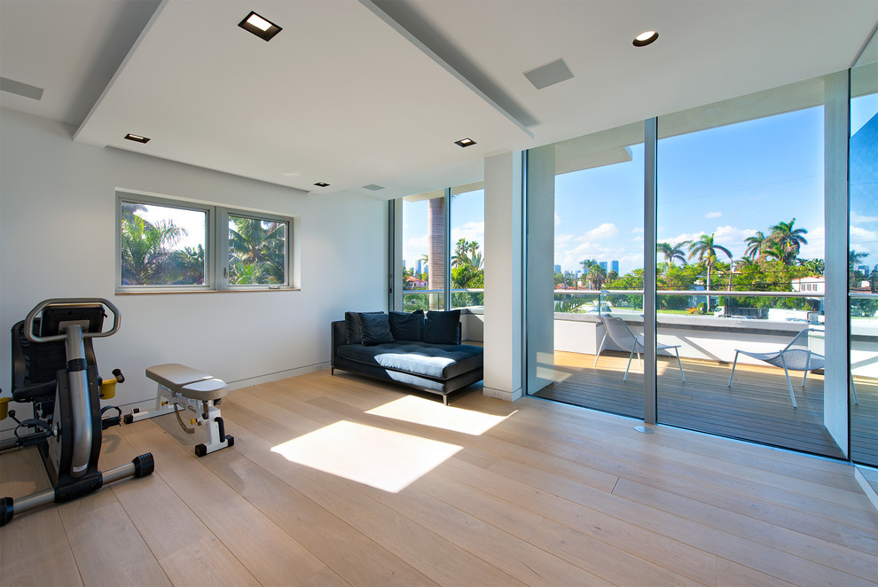 This is an example of a contemporary multi-use home gym in Miami with white walls, light hardwood flooring and beige floors.