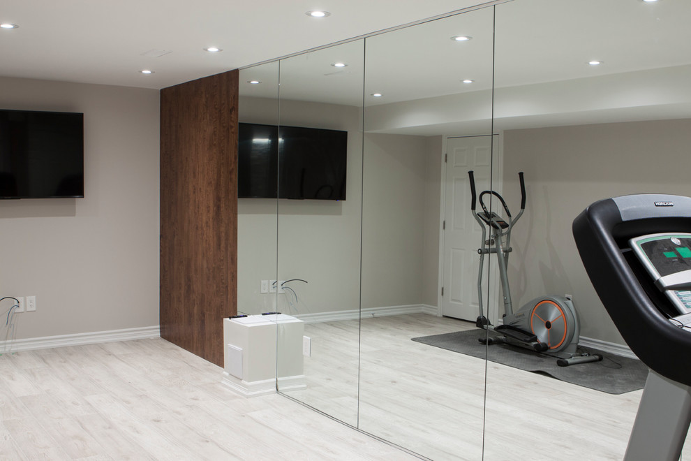 Imagen de sala de pesas minimalista grande con paredes grises, suelo laminado y suelo gris