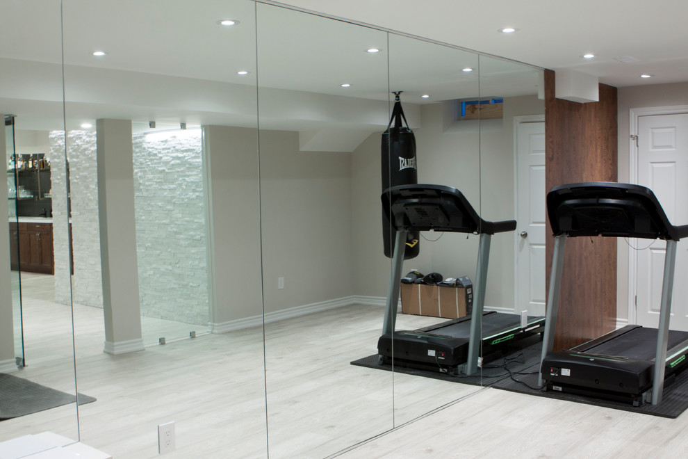 Modelo de sala de pesas moderna grande con paredes grises, suelo laminado y suelo gris