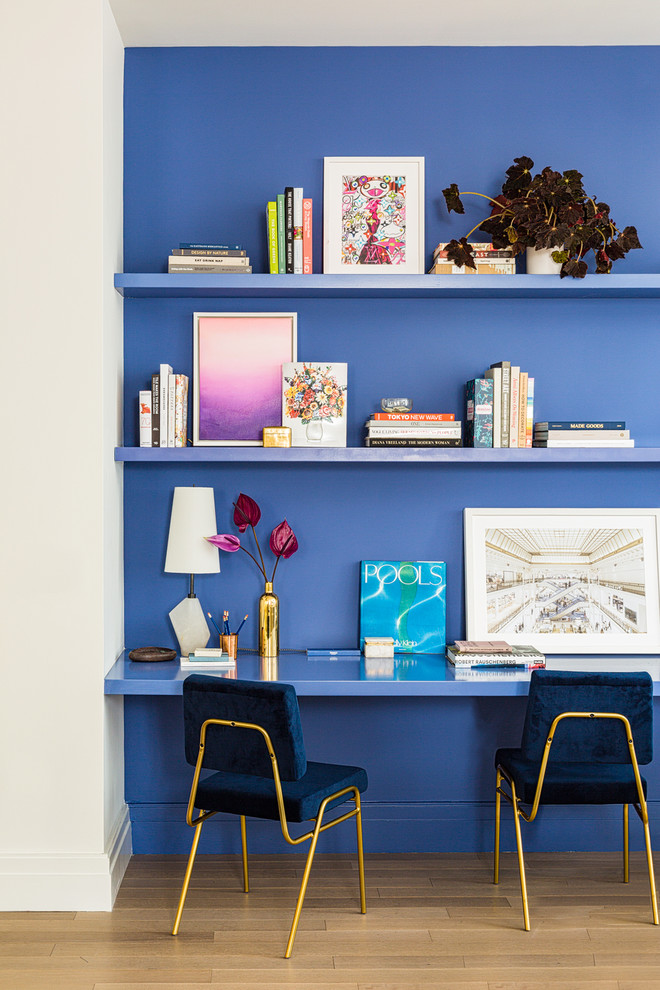 Diseño de despacho contemporáneo con paredes azules, suelo de madera clara, escritorio empotrado y suelo beige