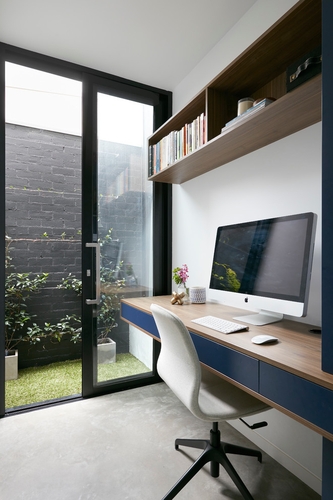 Ejemplo de despacho actual con paredes blancas, suelo de cemento y escritorio empotrado