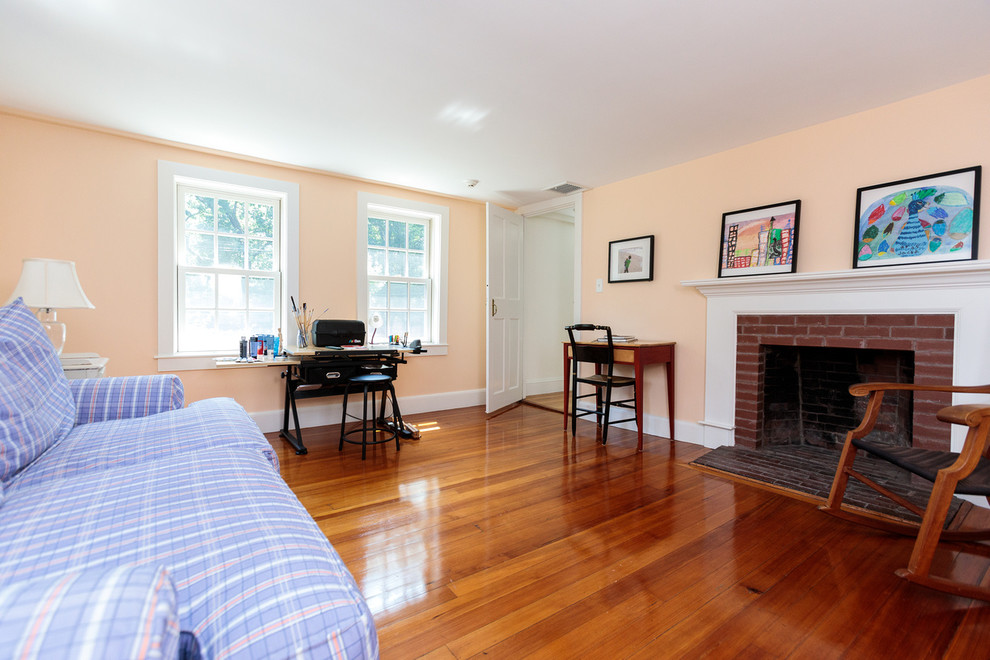 Mittelgroßes Klassisches Lesezimmer mit beiger Wandfarbe, braunem Holzboden, Kamin, Kaminumrandung aus Backstein und freistehendem Schreibtisch in Boston