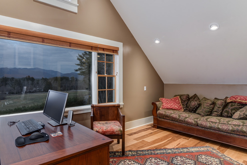 Modelo de despacho de estilo de casa de campo grande con paredes marrones, suelo de madera clara, escritorio independiente y chimenea de doble cara