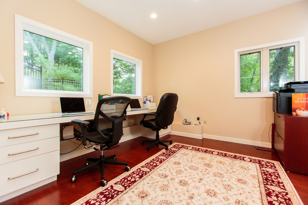 Modelo de estudio tradicional renovado de tamaño medio con paredes beige, suelo de madera en tonos medios y escritorio empotrado
