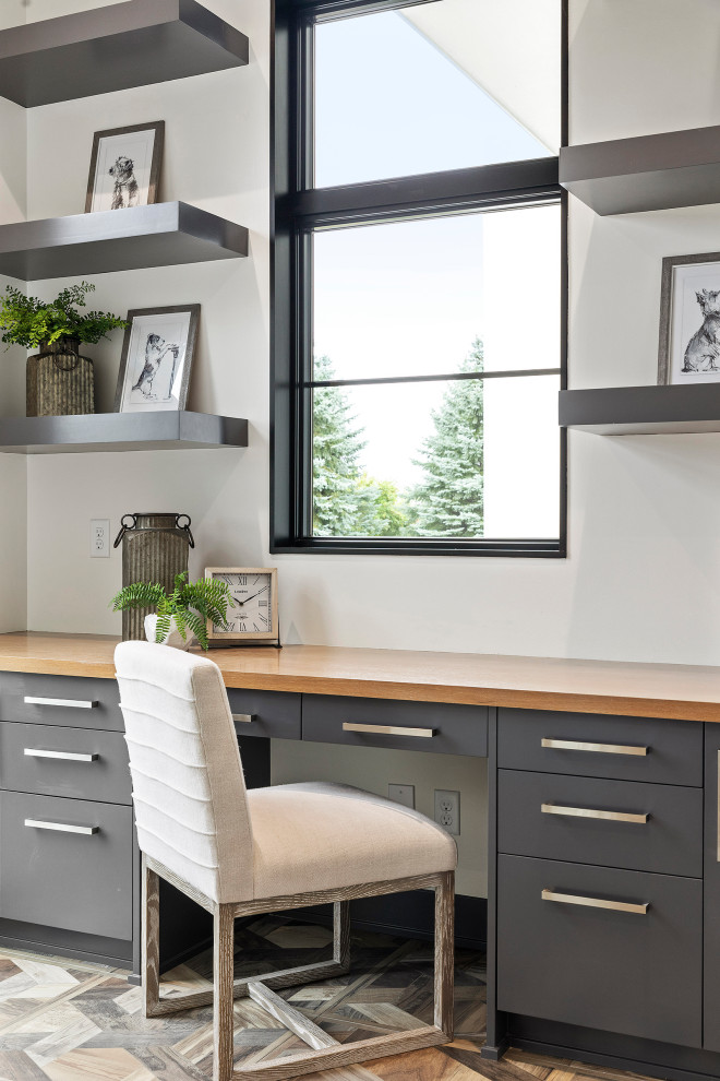 Modelo de despacho contemporáneo grande con paredes blancas, suelo de madera en tonos medios, escritorio empotrado y suelo marrón