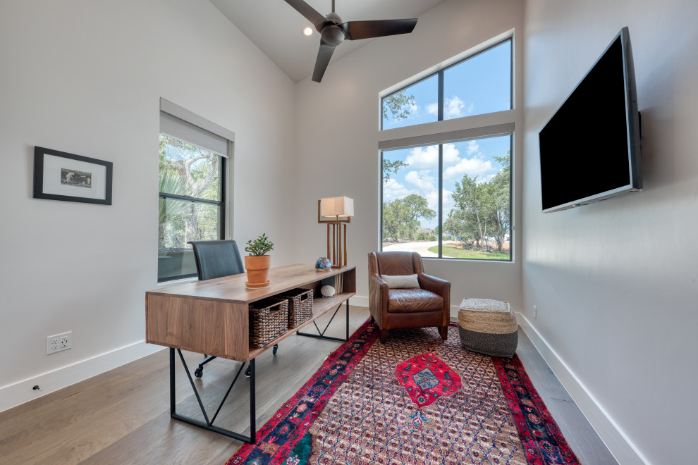 Mittelgroßes Modernes Arbeitszimmer ohne Kamin mit Arbeitsplatz, grauer Wandfarbe, braunem Holzboden, freistehendem Schreibtisch und braunem Boden in Austin