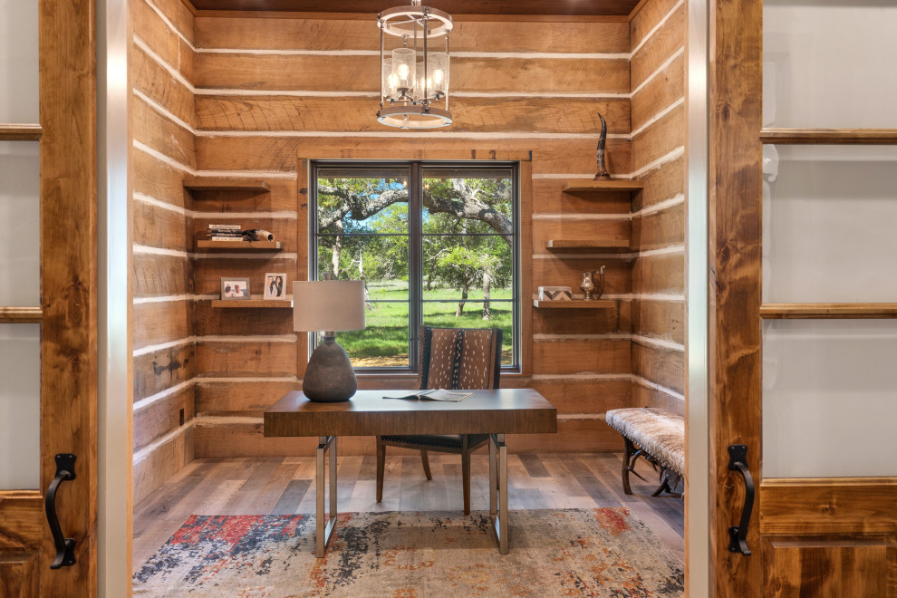 Mittelgroßes Landhaus Arbeitszimmer mit Arbeitsplatz, brauner Wandfarbe, hellem Holzboden, buntem Boden, Holzdecke und Holzwänden in Austin