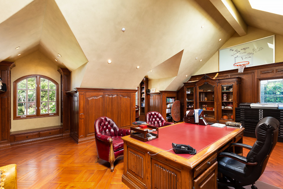 Aménagement d'un très grand bureau montagne avec une bibliothèque ou un coin lecture, un mur beige, un sol en bois brun, un bureau indépendant et un sol marron.
