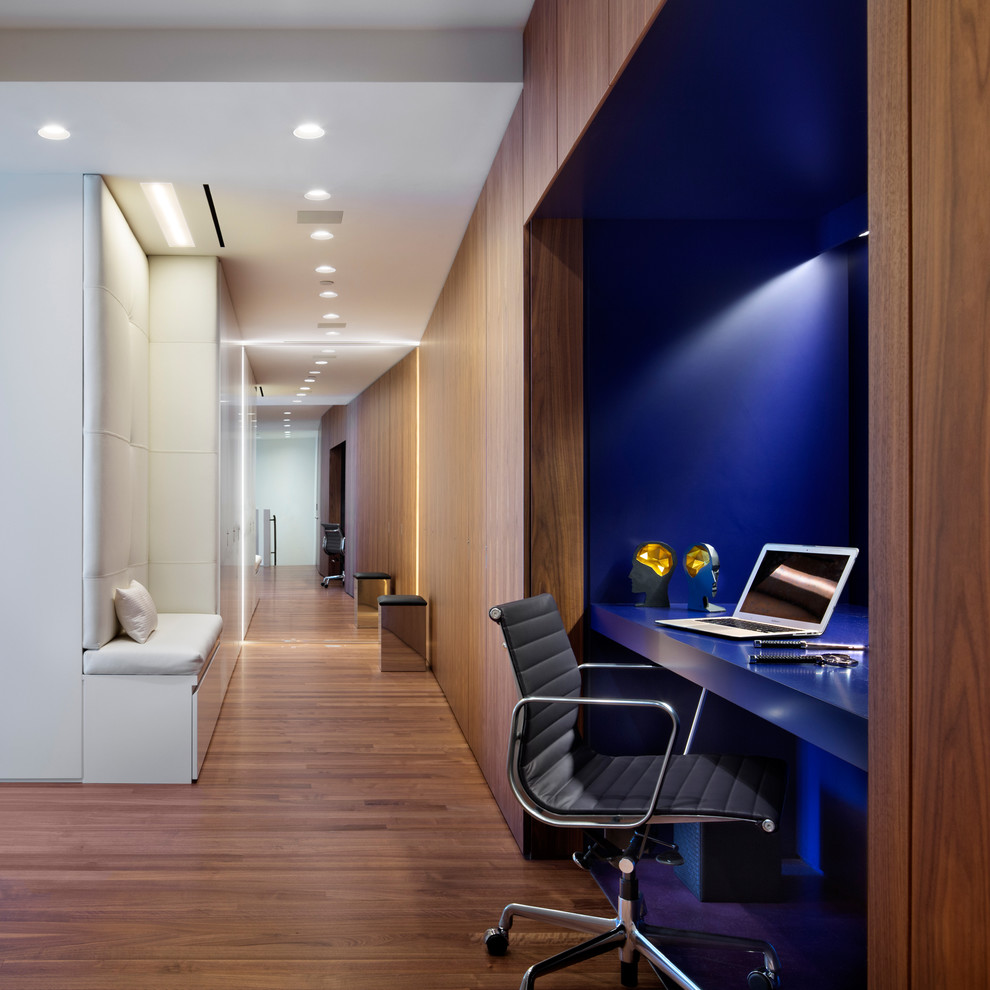 Ejemplo de despacho actual con paredes azules, suelo de madera en tonos medios y escritorio empotrado