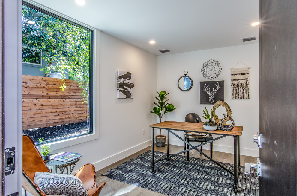 Landhaus Arbeitszimmer mit Arbeitsplatz, weißer Wandfarbe, hellem Holzboden, freistehendem Schreibtisch und beigem Boden in Austin