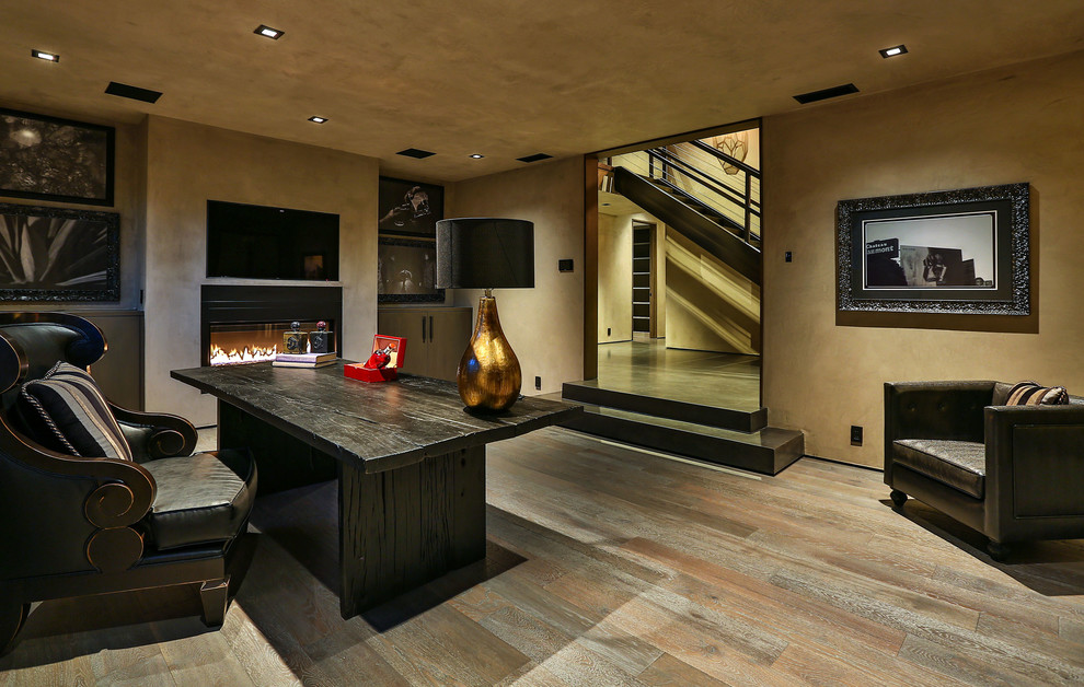 Mittelgroßes Modernes Arbeitszimmer mit Arbeitsplatz, beiger Wandfarbe, hellem Holzboden, Gaskamin, Kaminumrandung aus Beton, freistehendem Schreibtisch und braunem Boden in Los Angeles