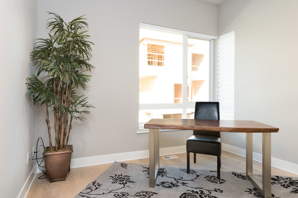 Modelo de despacho tradicional renovado pequeño sin chimenea con paredes beige, suelo de madera clara, escritorio independiente y suelo beige