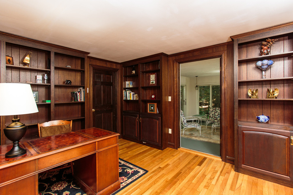 Bild på ett mellanstort vintage hemmabibliotek, med bruna väggar, mellanmörkt trägolv och ett fristående skrivbord