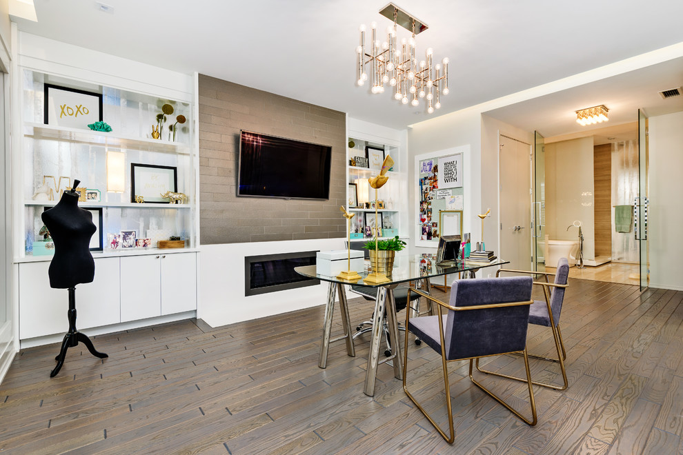 This is an example of a contemporary study in Chicago with white walls, a ribbon fireplace, a metal fireplace surround, a freestanding desk and brown floors.