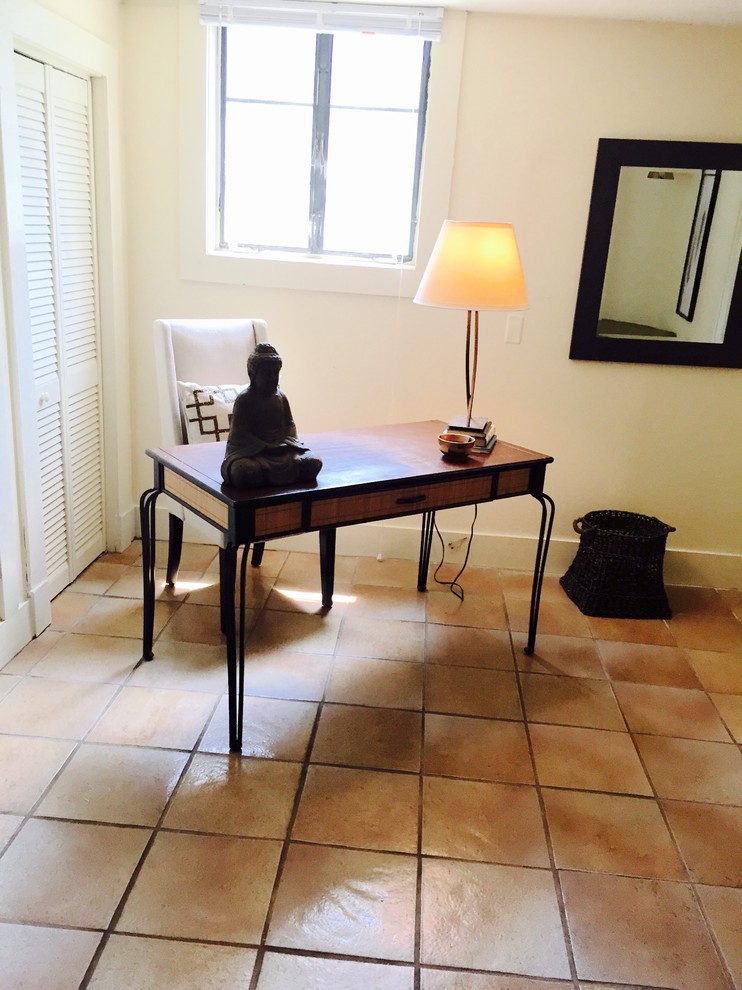 Modelo de despacho ecléctico de tamaño medio sin chimenea con paredes blancas, suelo de baldosas de terracota y escritorio independiente