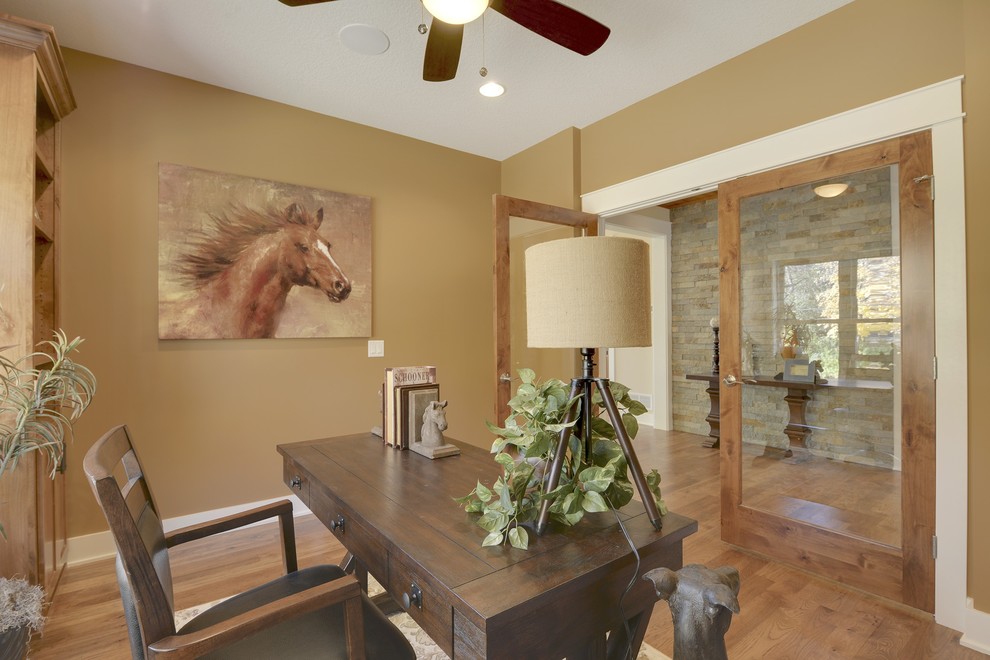 Landhaus Arbeitszimmer mit Arbeitsplatz, brauner Wandfarbe, braunem Holzboden, freistehendem Schreibtisch und braunem Boden in Minneapolis