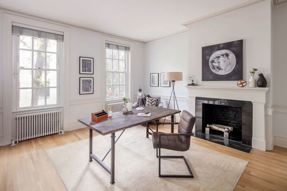 This is an example of a classic study in New York with a freestanding desk, grey walls, light hardwood flooring, a standard fireplace and a chimney breast.