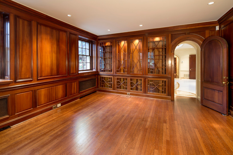 Ejemplo de despacho tradicional grande sin chimenea con paredes marrones y suelo de madera en tonos medios