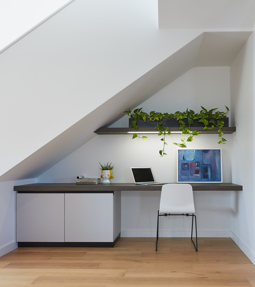 Imagen de despacho contemporáneo de tamaño medio con paredes blancas, suelo de madera clara, escritorio empotrado y suelo beige