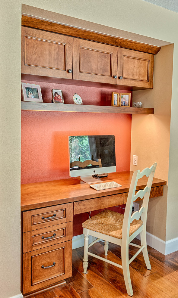 Aménagement d'un petit bureau campagne avec un mur orange, un sol en bois brun, un bureau intégré et un sol marron.