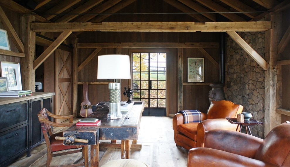 Lantlig inredning av ett mellanstort arbetsrum, med en öppen vedspis, ett fristående skrivbord, bruna väggar och ljust trägolv