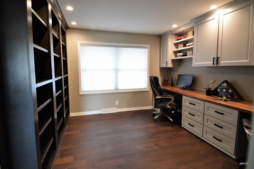 Cette photo montre un grand bureau tendance avec un mur beige, parquet foncé, aucune cheminée, un bureau intégré et un sol marron.