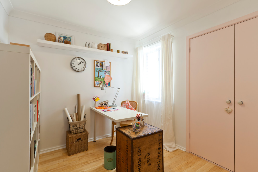 Inredning av ett eklektiskt litet hobbyrum, med vita väggar, ljust trägolv och ett fristående skrivbord