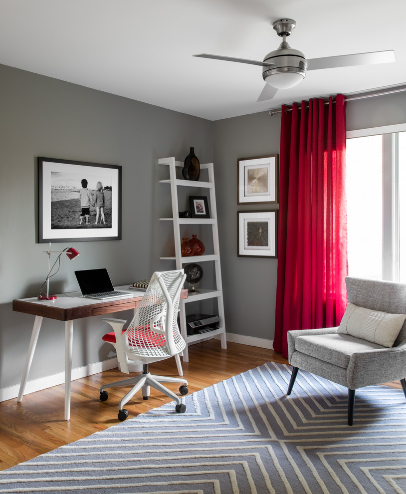 Mittelgroßes Modernes Arbeitszimmer mit grauer Wandfarbe, braunem Holzboden, Arbeitsplatz und freistehendem Schreibtisch in New York