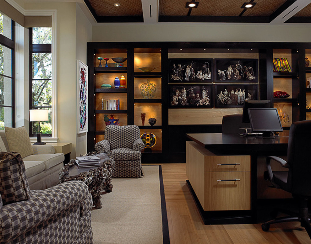 Diseño de despacho actual grande sin chimenea con paredes beige, suelo de madera clara y escritorio independiente