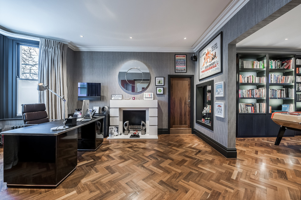 Modelo de despacho clásico renovado con paredes grises, suelo de madera en tonos medios, todas las chimeneas y escritorio independiente