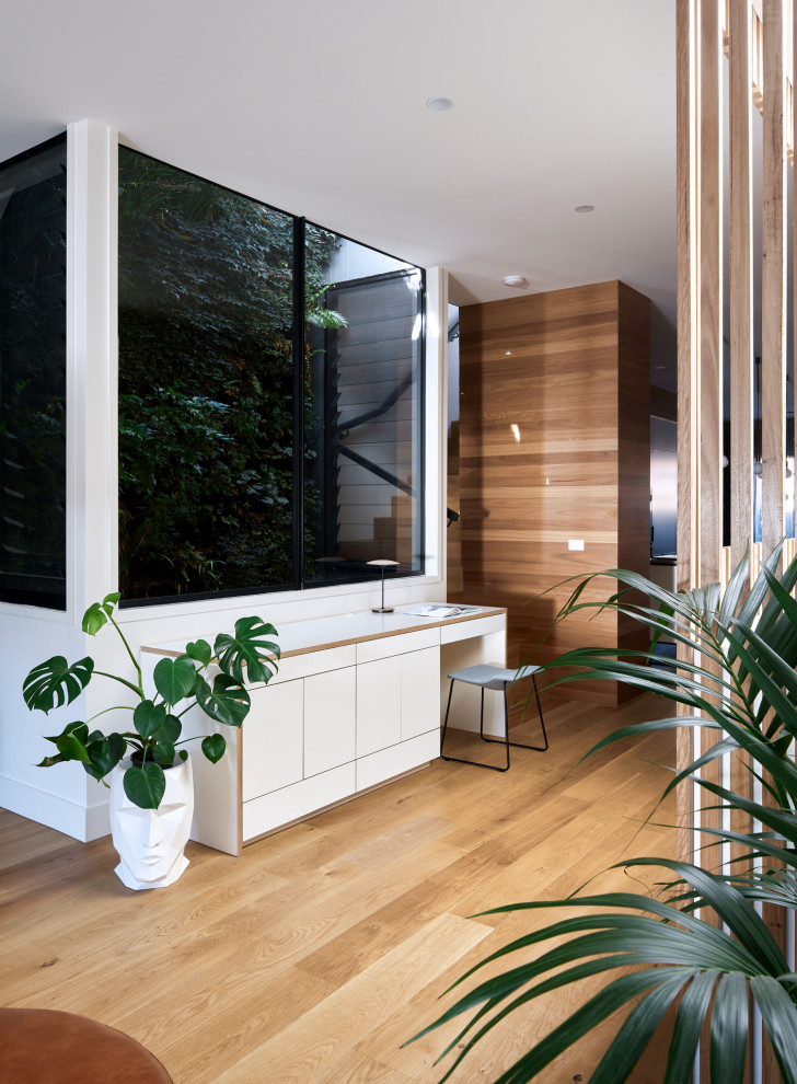 Mittelgroßes Modernes Arbeitszimmer mit weißer Wandfarbe, hellem Holzboden, Einbau-Schreibtisch und braunem Boden in Melbourne