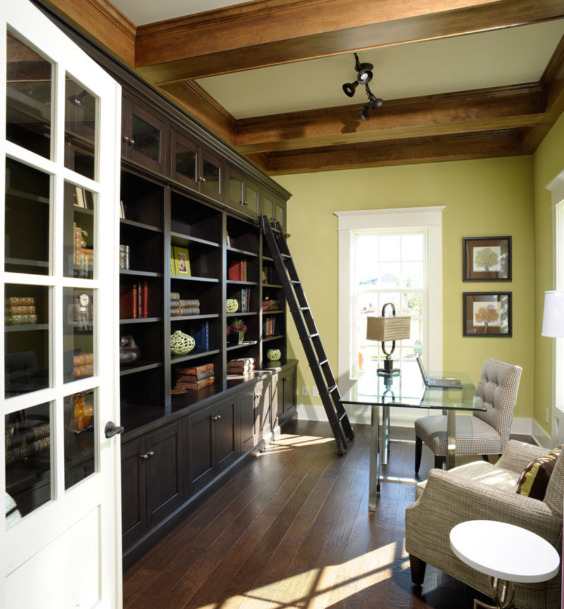 На фото: домашняя библиотека в классическом стиле с зелеными стенами, темным паркетным полом, отдельно стоящим рабочим столом и балками на потолке