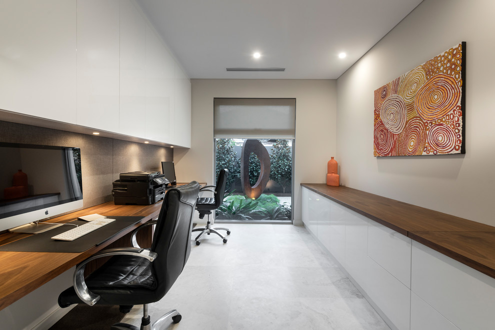 Modelo de despacho actual grande sin chimenea con paredes grises, suelo de piedra caliza, escritorio empotrado y suelo gris