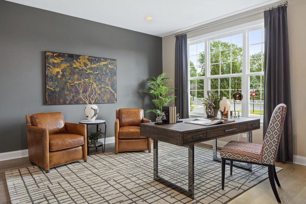 Landhaus Arbeitszimmer mit grauer Wandfarbe, braunem Holzboden, freistehendem Schreibtisch und braunem Boden in Indianapolis